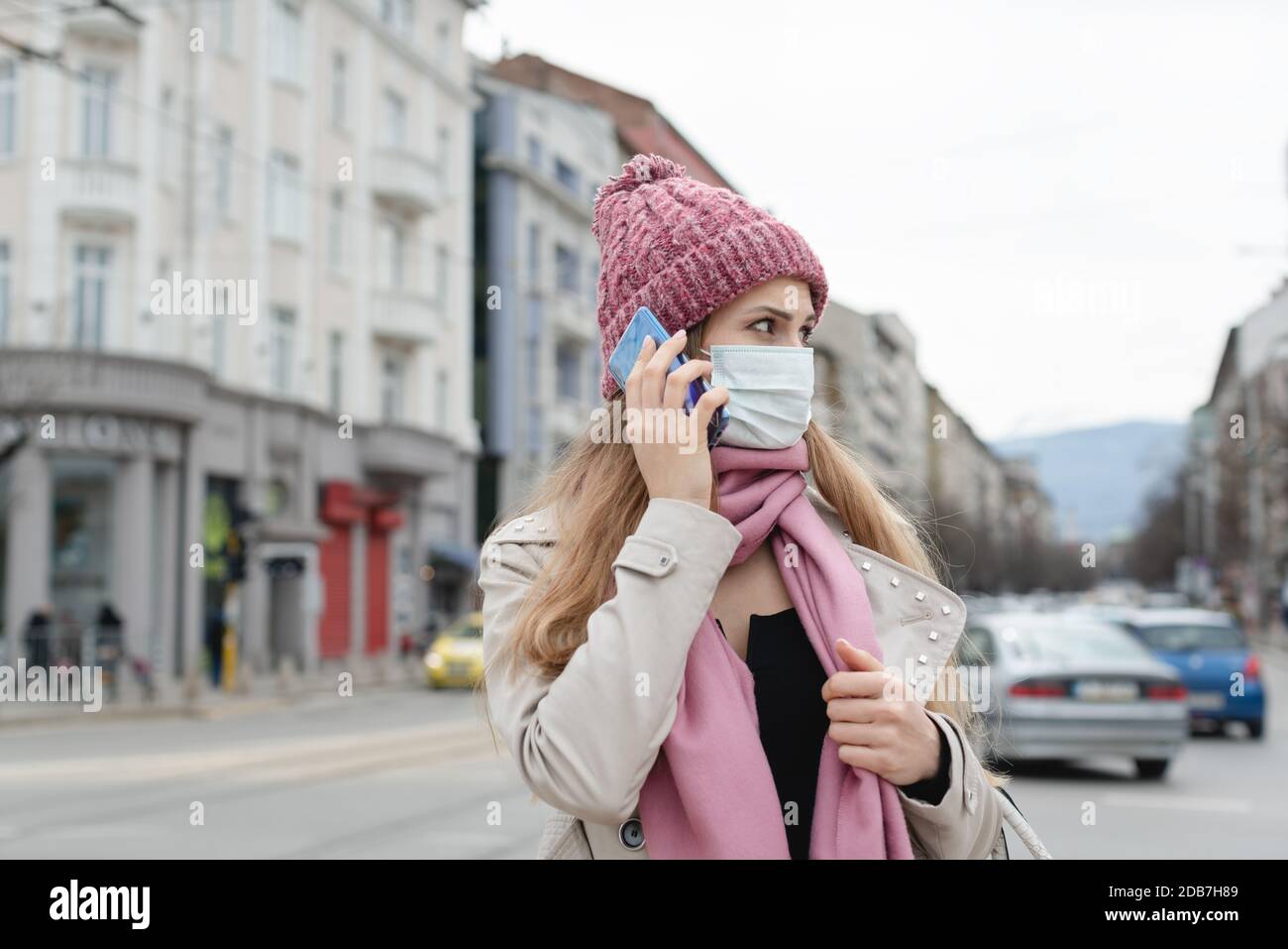 Concerned woman using her phone wearing medical mask and gloves in city Stock Photo