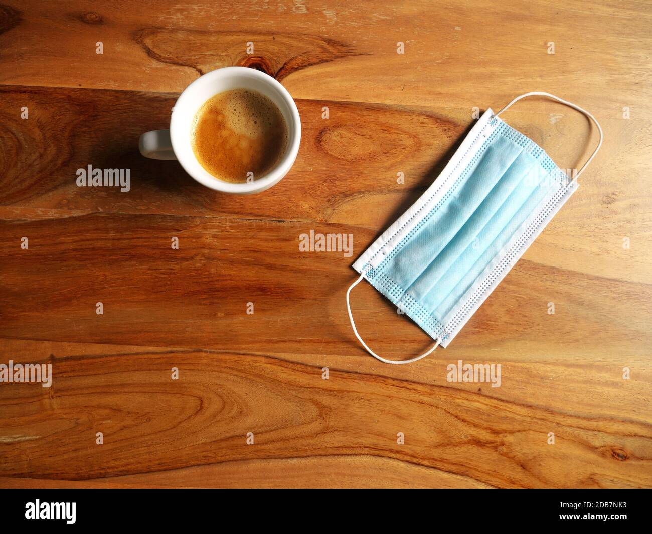 Coffee cup placed on a wooden table next to a mask. Top view Stock Photo