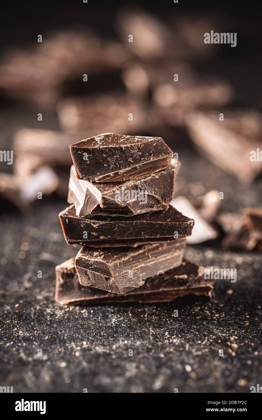 Pieces of chocolate bar. Broken dark chocolate on black table. Stock Photo