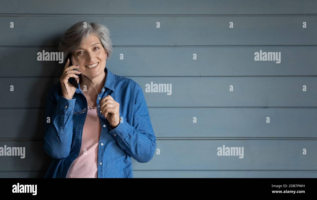 Smiling mature woman talking on phone on grey wall background Stock Photo