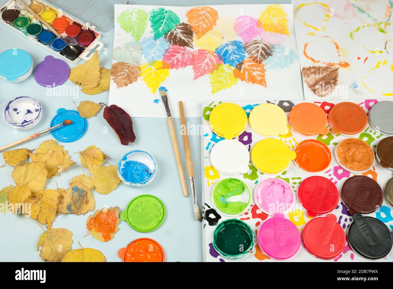 Finger paints and watercolors on the child table. Painted autumn tree leaves imprinted on the paper.  Toys for encouraging creativity of children. Stock Photo