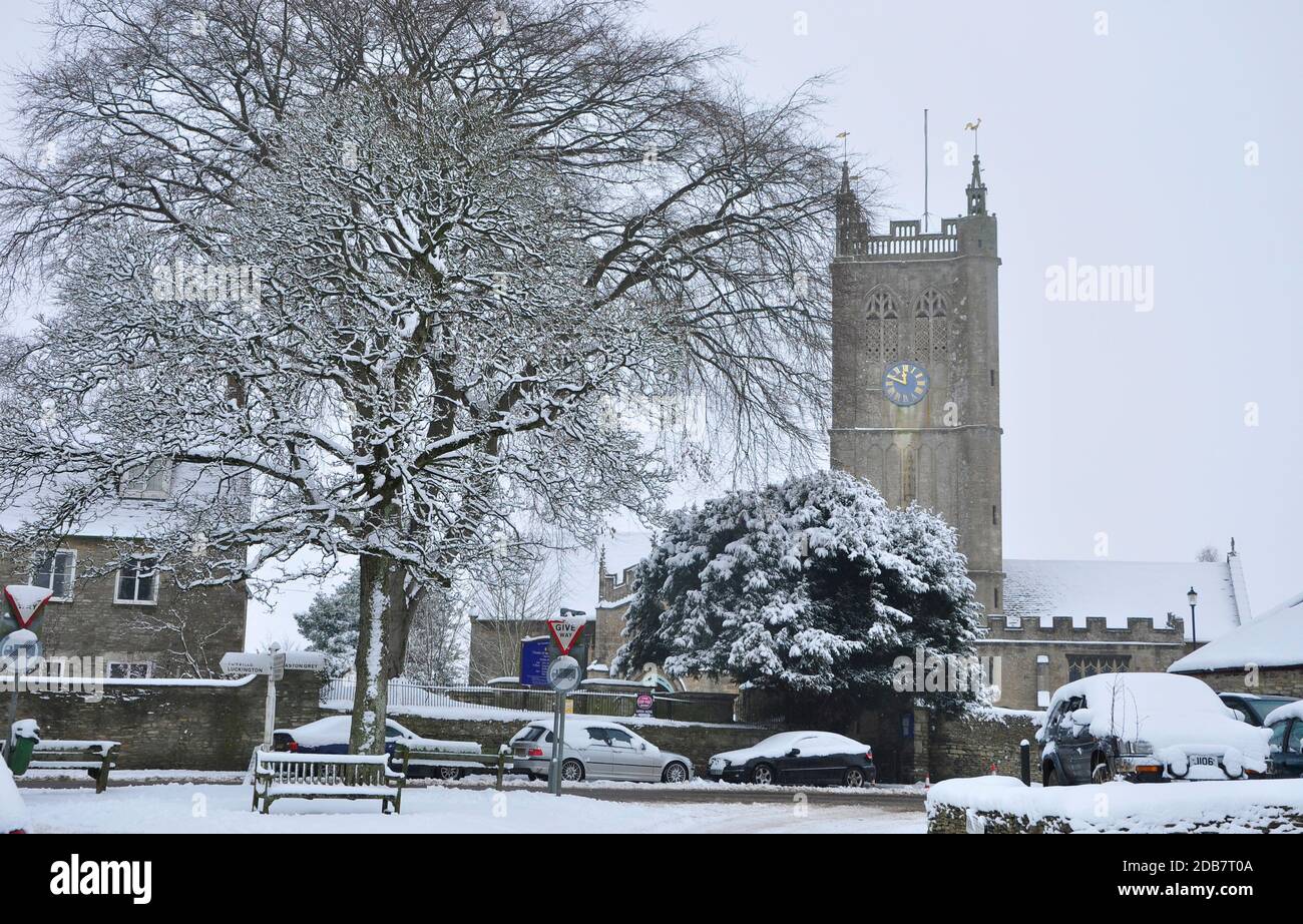 A snowy scene at Sherston in Wiltshire. The Church of the Holy Cross with vehicles and trees covered in snow.UK Stock Photo