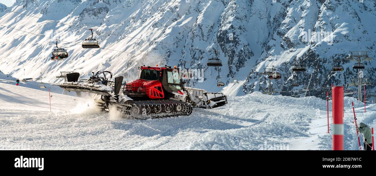 Red modern snowcat ratrack with snowplow snow grooming machine preparing ski slope piste hillalpine skiing winter resort Ischgl in Austria. Heavy Stock Photo