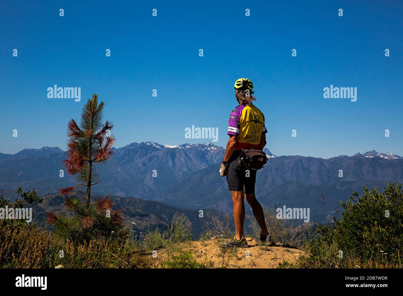 WA18136-00...WASHINGTON - Cyclist checking out the view from turnout along the Chumshick Mountain Road with Mount Stuart and Little Annapurna in view Stock Photo