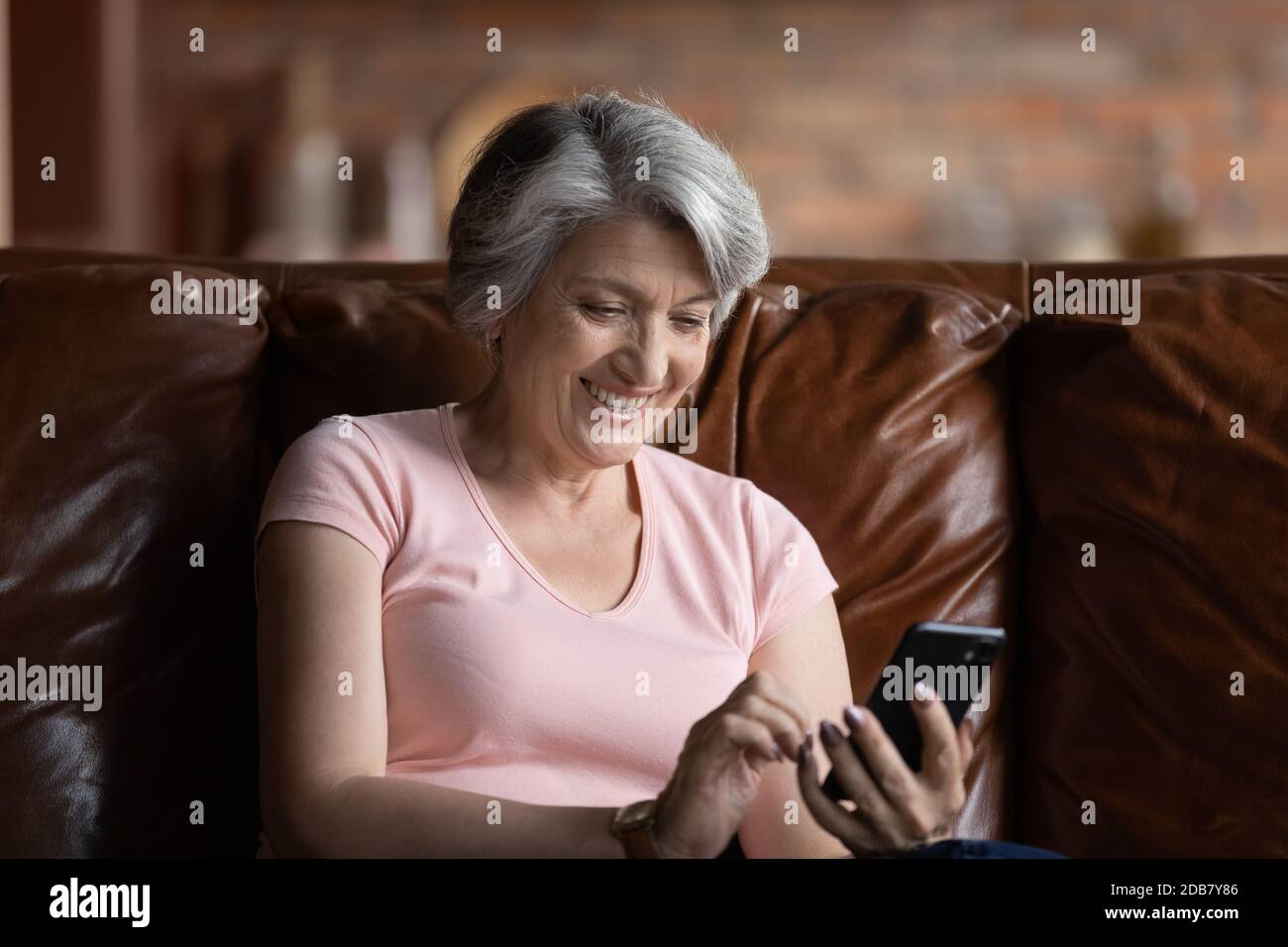 Smiling mature woman holding smartphone, surfing internet at home Stock Photo