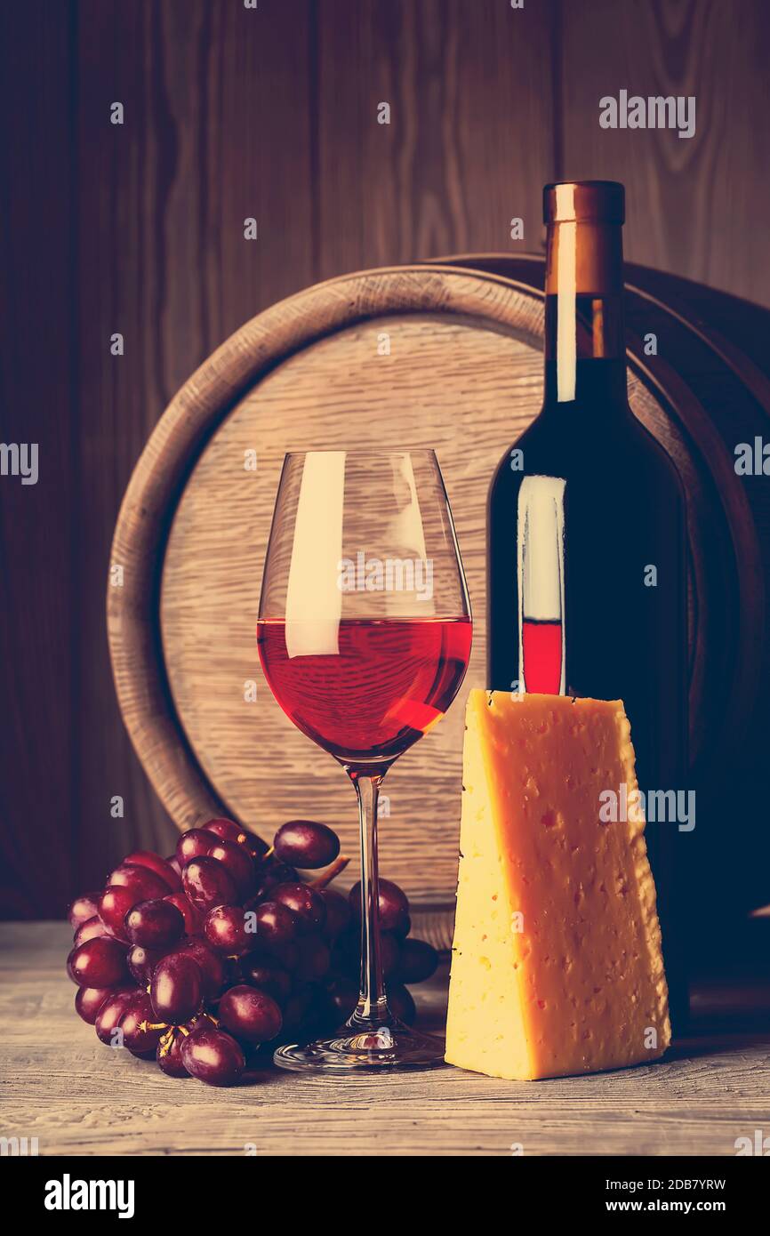 Bottle and glass of red wine with cheese on a background of the barrel