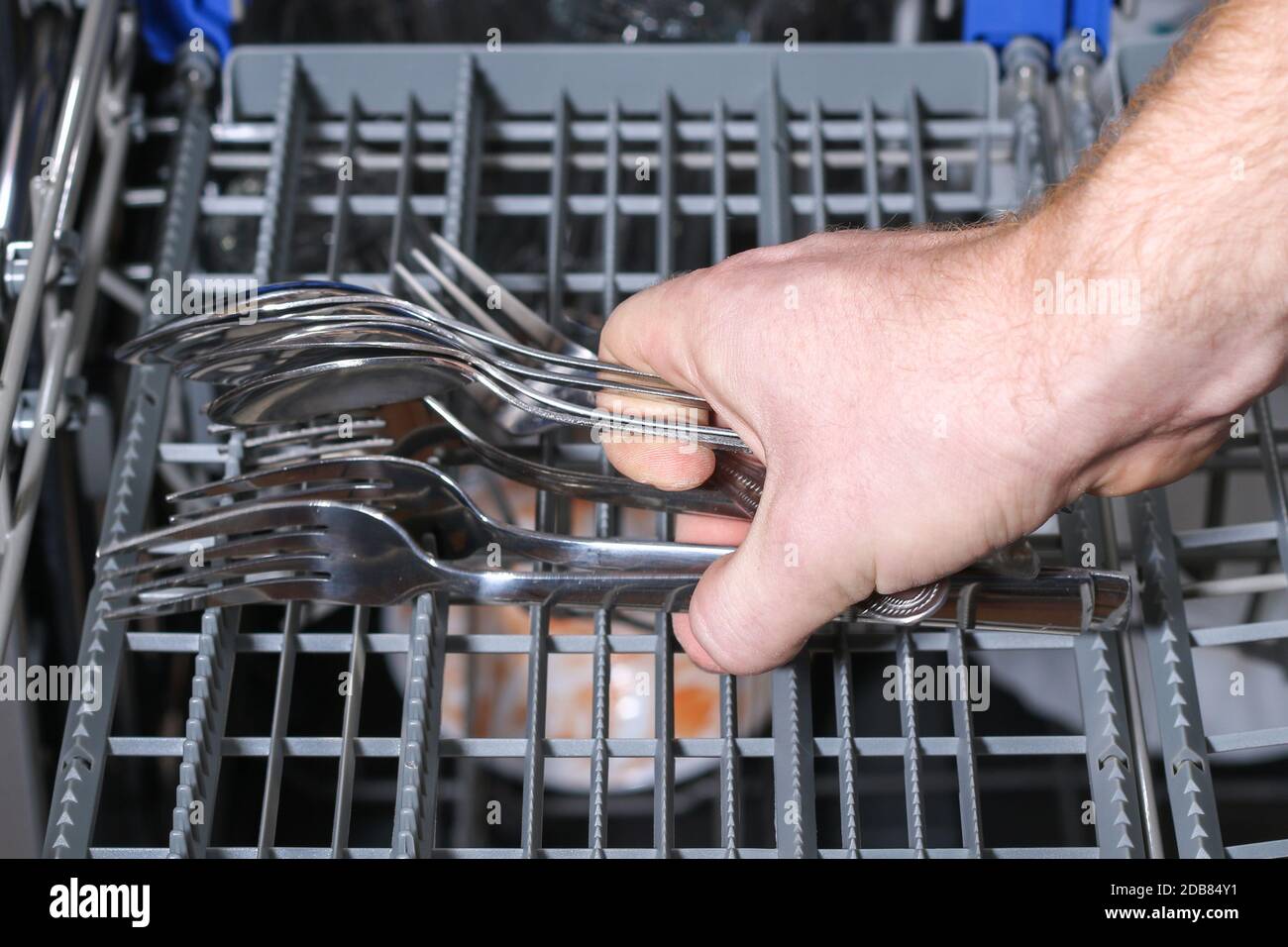 A man loads dirty dishes, plates, spoons, forks, cutlery into the