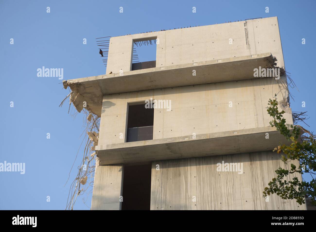 Plain blue background behind the top three floors of an empty concrete building. Partly wrecked and demolished as steel supports hang out with rubble Stock Photo