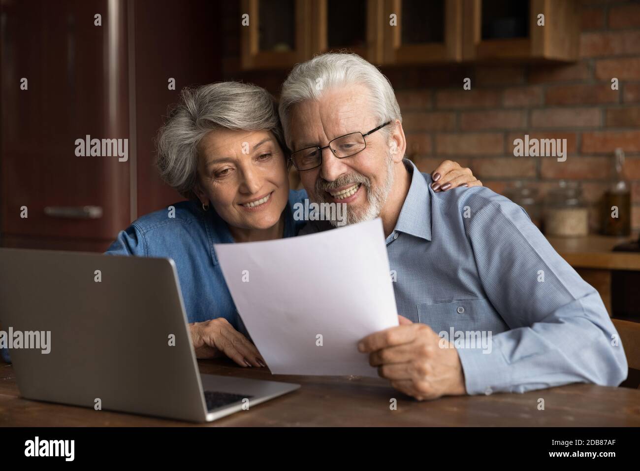 Smiling mature couple reading letter with good news, using laptop Stock Photo