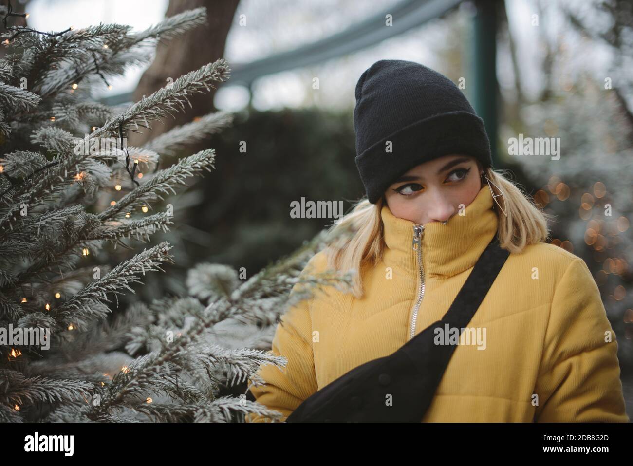 Portrait of a young woman in a puffer jacket standing by a Christmas tree, France Stock Photo