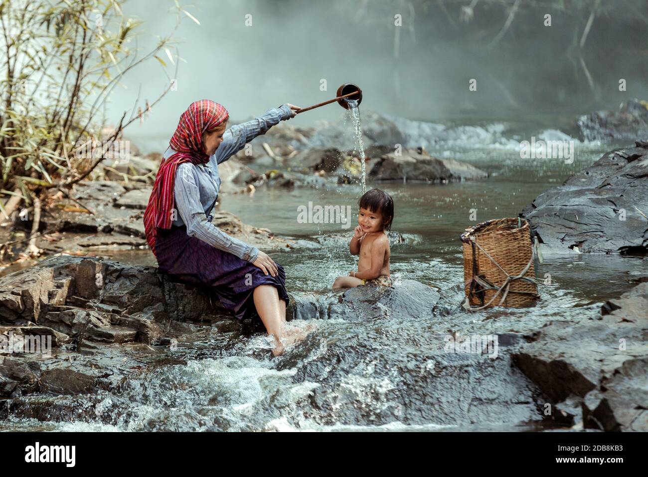 Mother sitting by a river bathing her daughter, Thailand Stock Photo