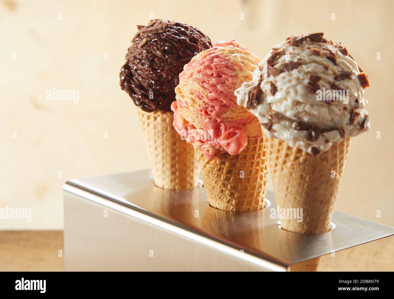 Three ice cream cones with assorted flavors including chocolate, strawberry and choc chip standing in a metal holder on a counter Stock Photo