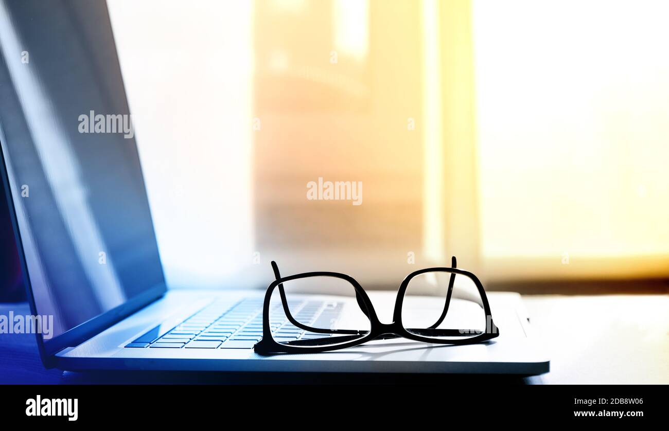 open laptop on which lie reading glasses in black frames Stock Photo