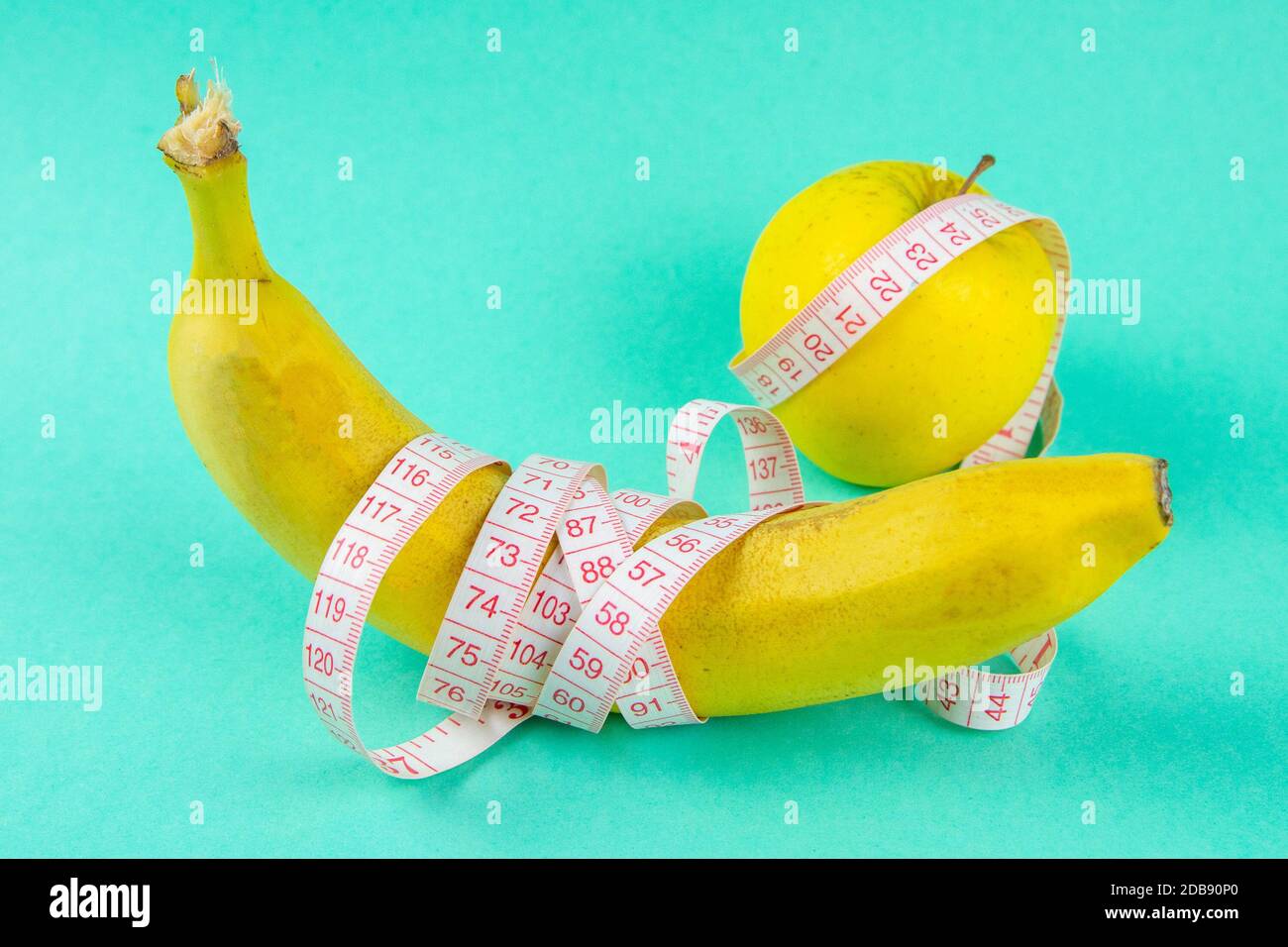 Different types of fruit, such as apples and bananas lie on a single-footed base and are wrapped in a measuring tape - concept for healthy weight loss Stock Photo