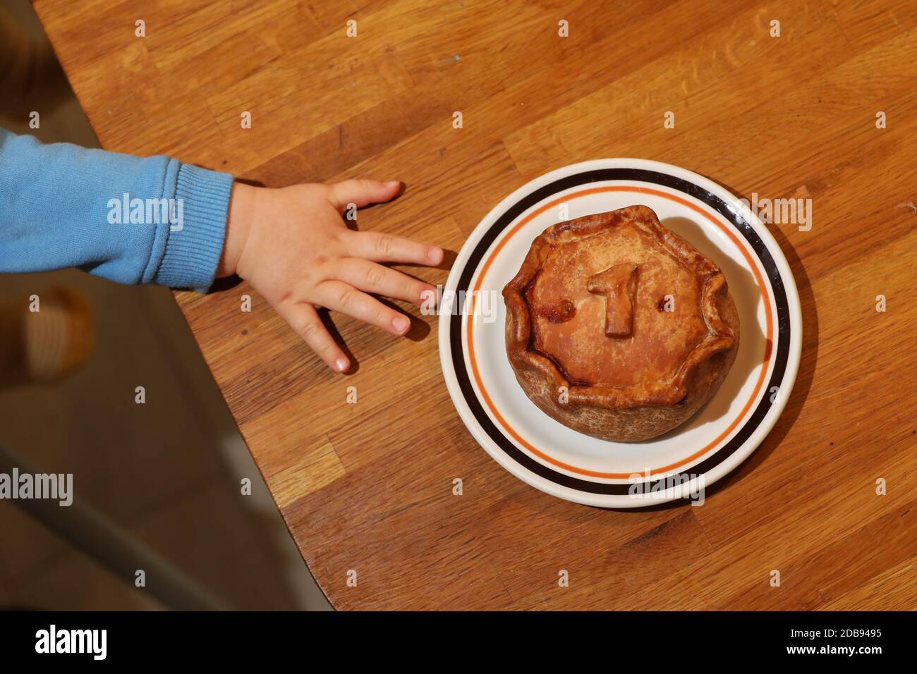A one year old trying to reach and take a No1 Melton Mowbray Pork Pie pictured in Sussex, UK. Stock Photo