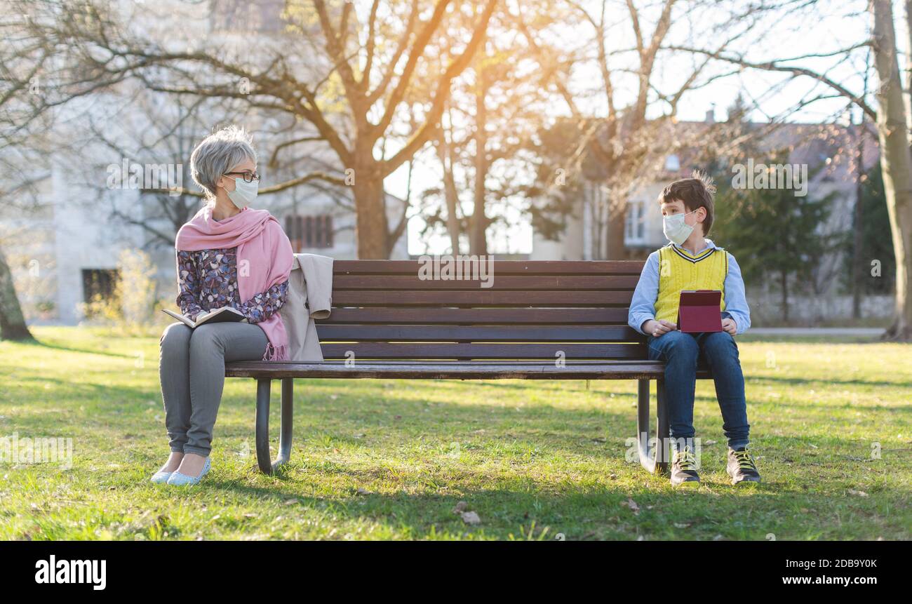 Grandmother and grandson separated by social distancing on park bench Stock Photo