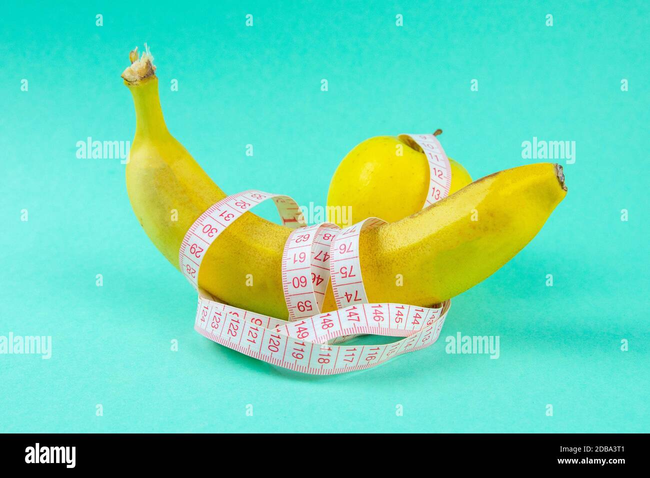 Different types of fruit, such as apples and bananas lie on a single-footed base and are wrapped in a measuring tape - concept for healthy weight loss Stock Photo