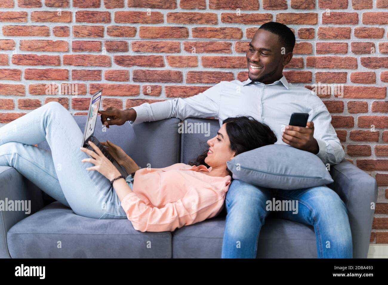 Couple Using Laptops While Relaxing On Sofa At Home Stock Photo