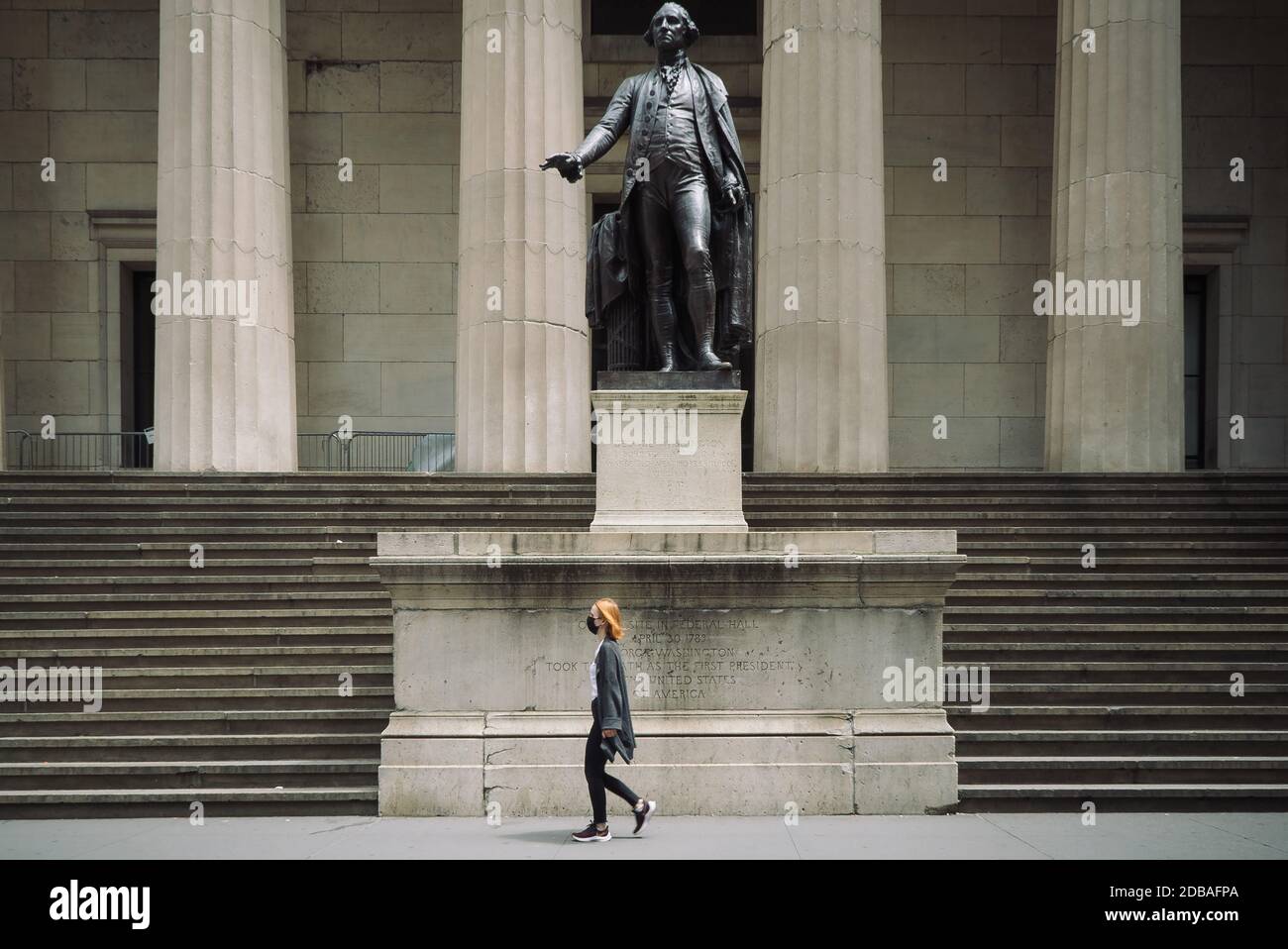 A woman wearing a face mask walks in front of John Quincy Adams Ward's bronze Statue of George Washington at Federal Hall in Wall street Stock Photo