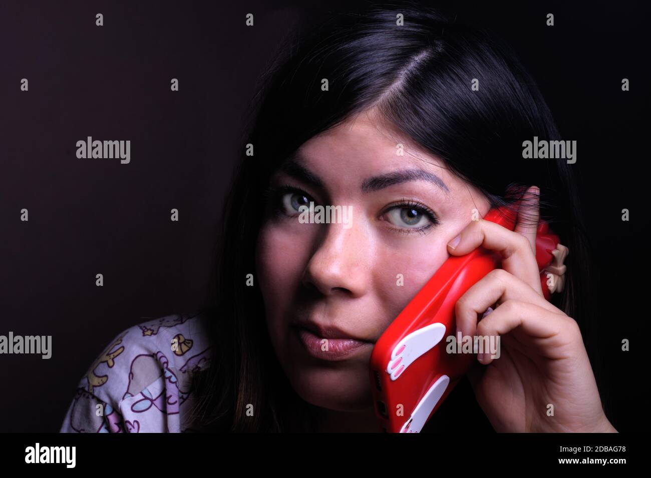 beautiful brunette girl with green eyes talking on a cell phone in a red case Stock Photo