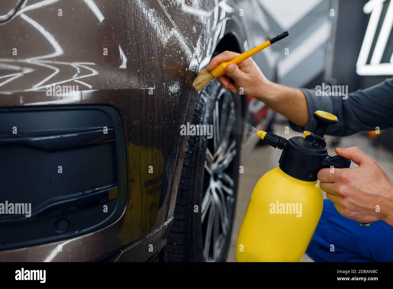 Male worker cleans car surface with spray and brush, preparation before ...