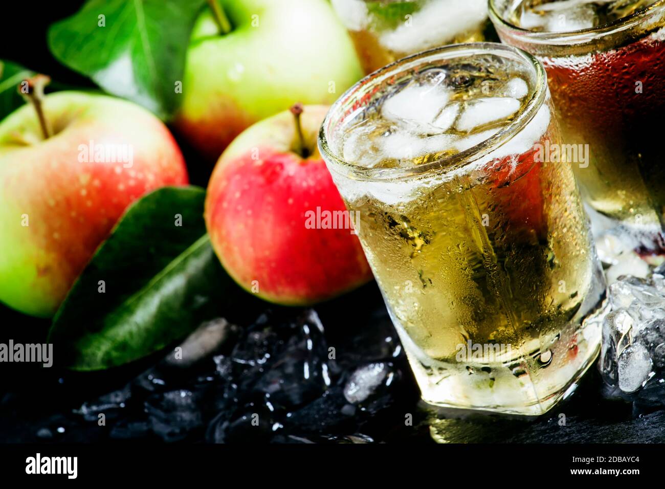 Cold apple juice with crushed ice, fresh apples with green leaves on a dark background, selective focus Stock Photo