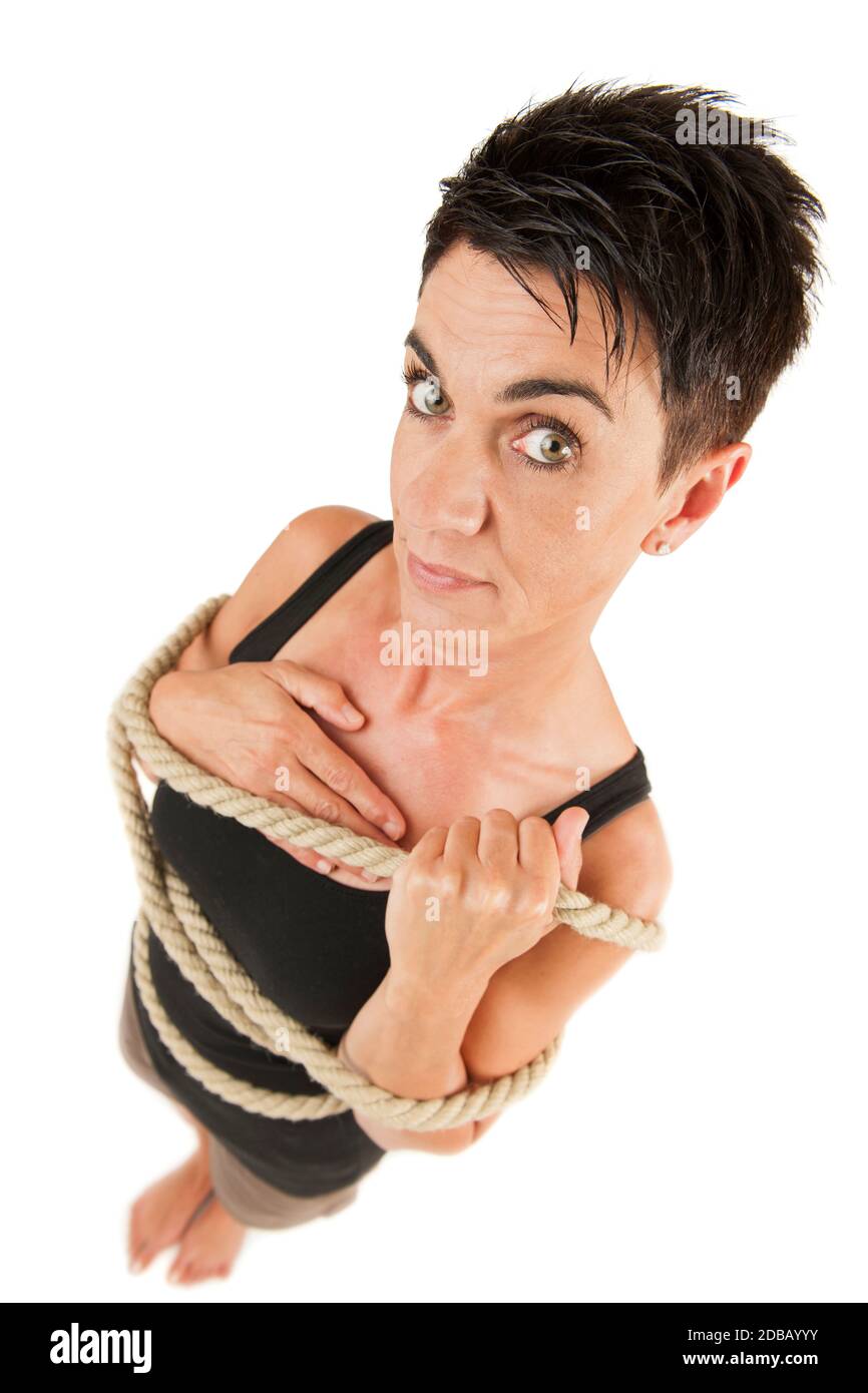 Wide-angle full-body view of a middle-aged black-haired woman from an elevated camera position with a rope around her body, looking seriously at the c Stock Photo