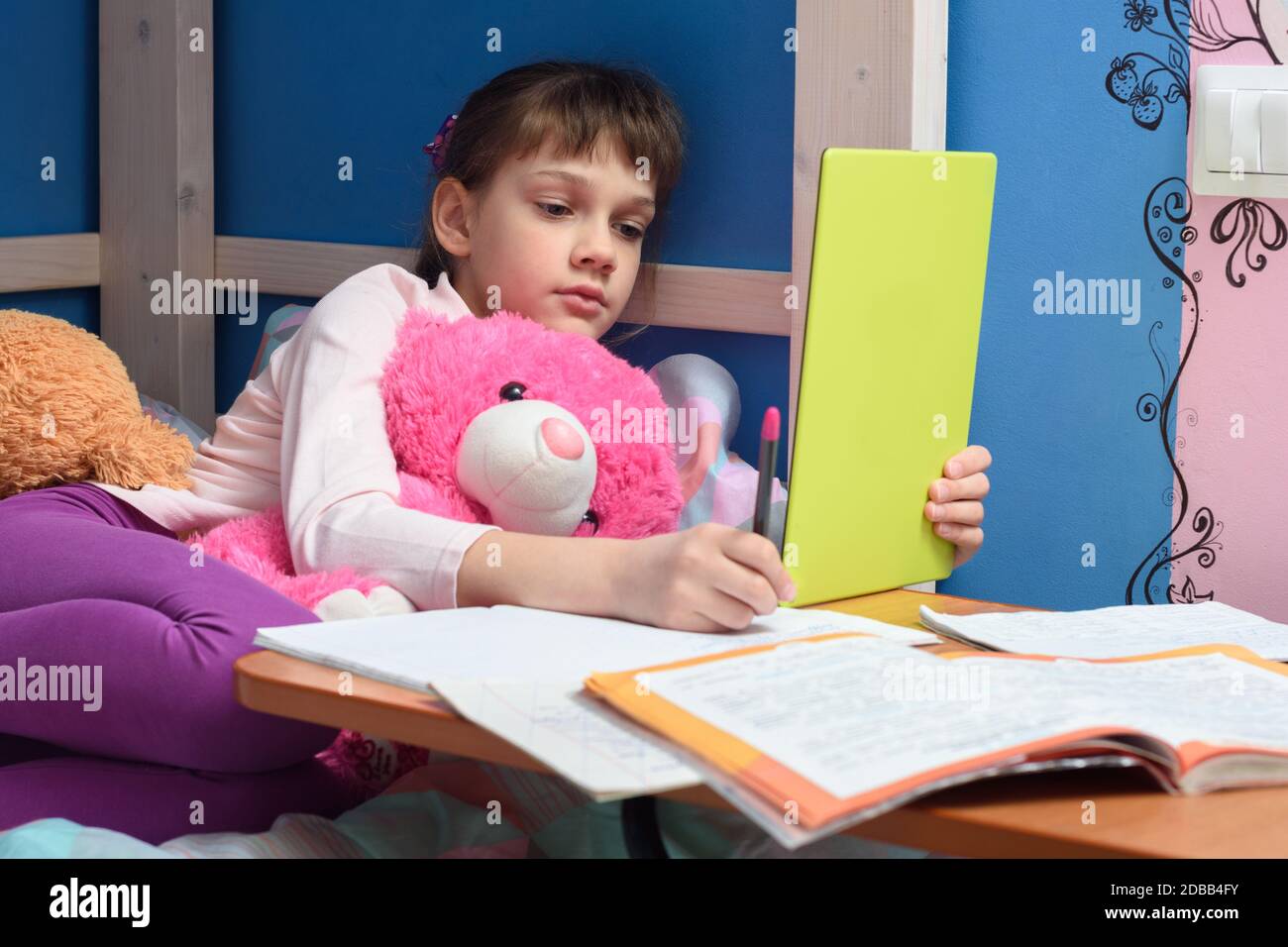Girl in the evening does homework at home using a tablet computer. Stock Photo