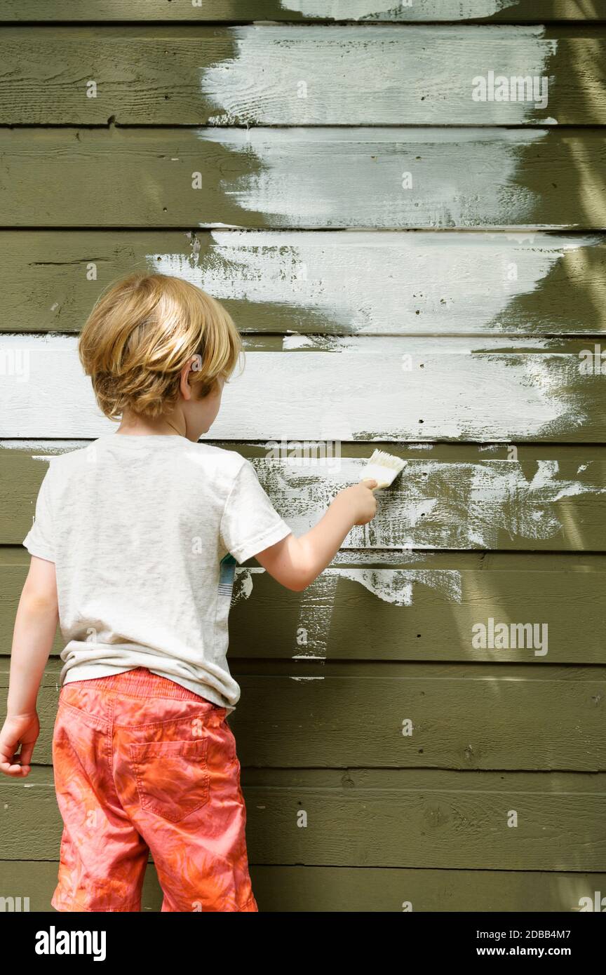 Boy (4-5) painting cottage wall Stock Photo