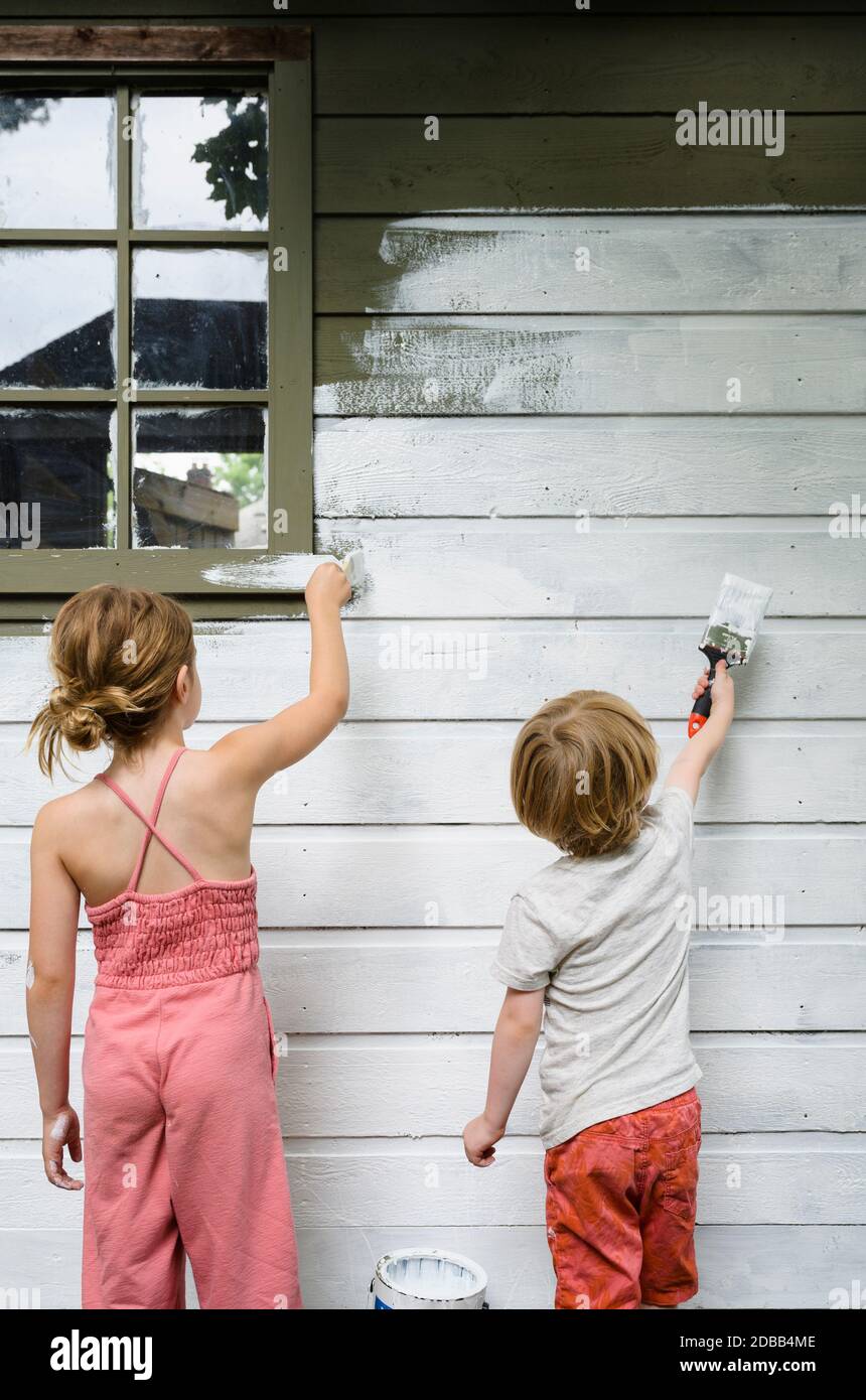 Girl (6-7) and boy (4-5) painting cottage wall Stock Photo