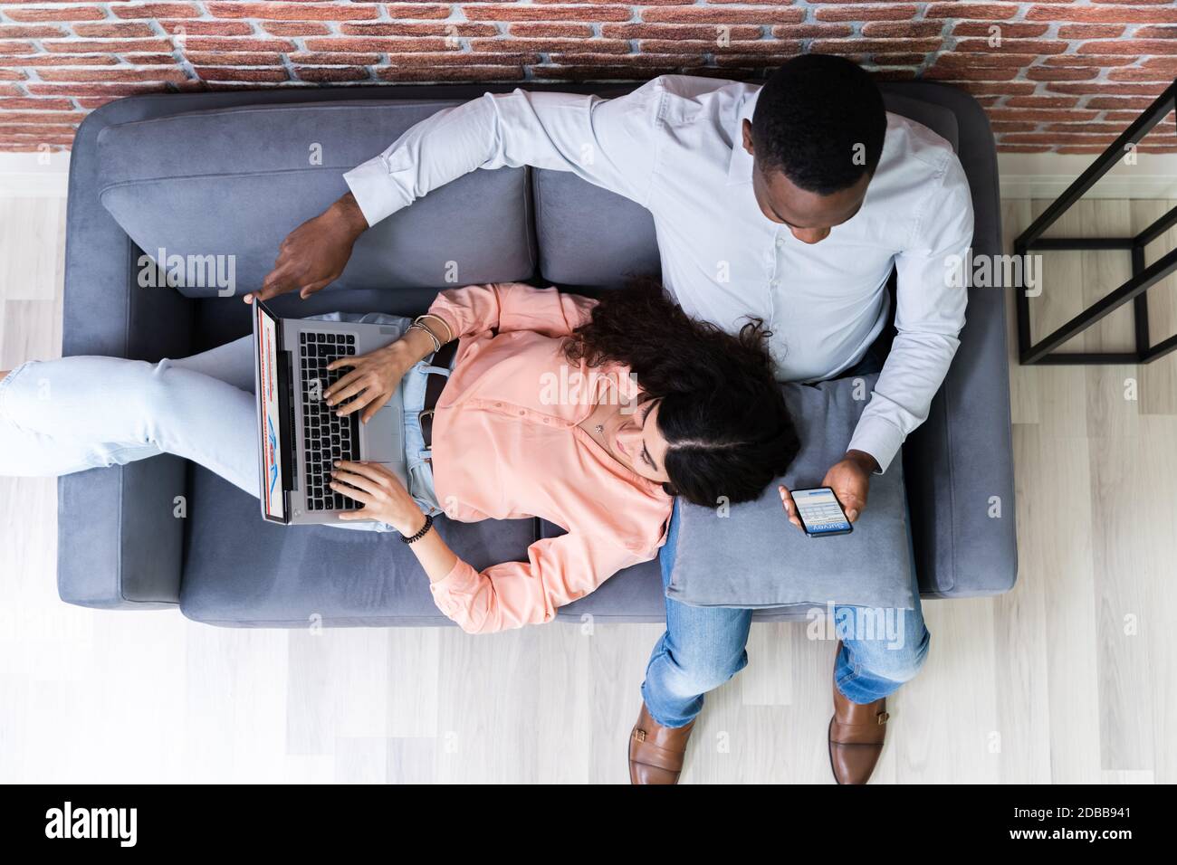 Couple Using Laptops While Relaxing On Sofa At Home Stock Photo