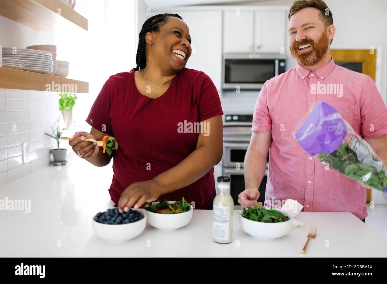 Happy man and woman preparing salad in kitchen Stock Photo