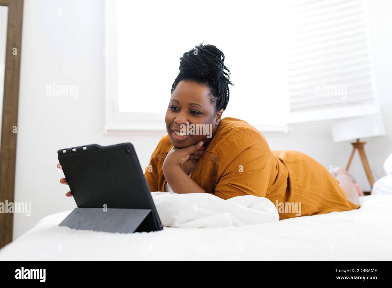 Smiling woman lying on bed and using tablet Stock Photo