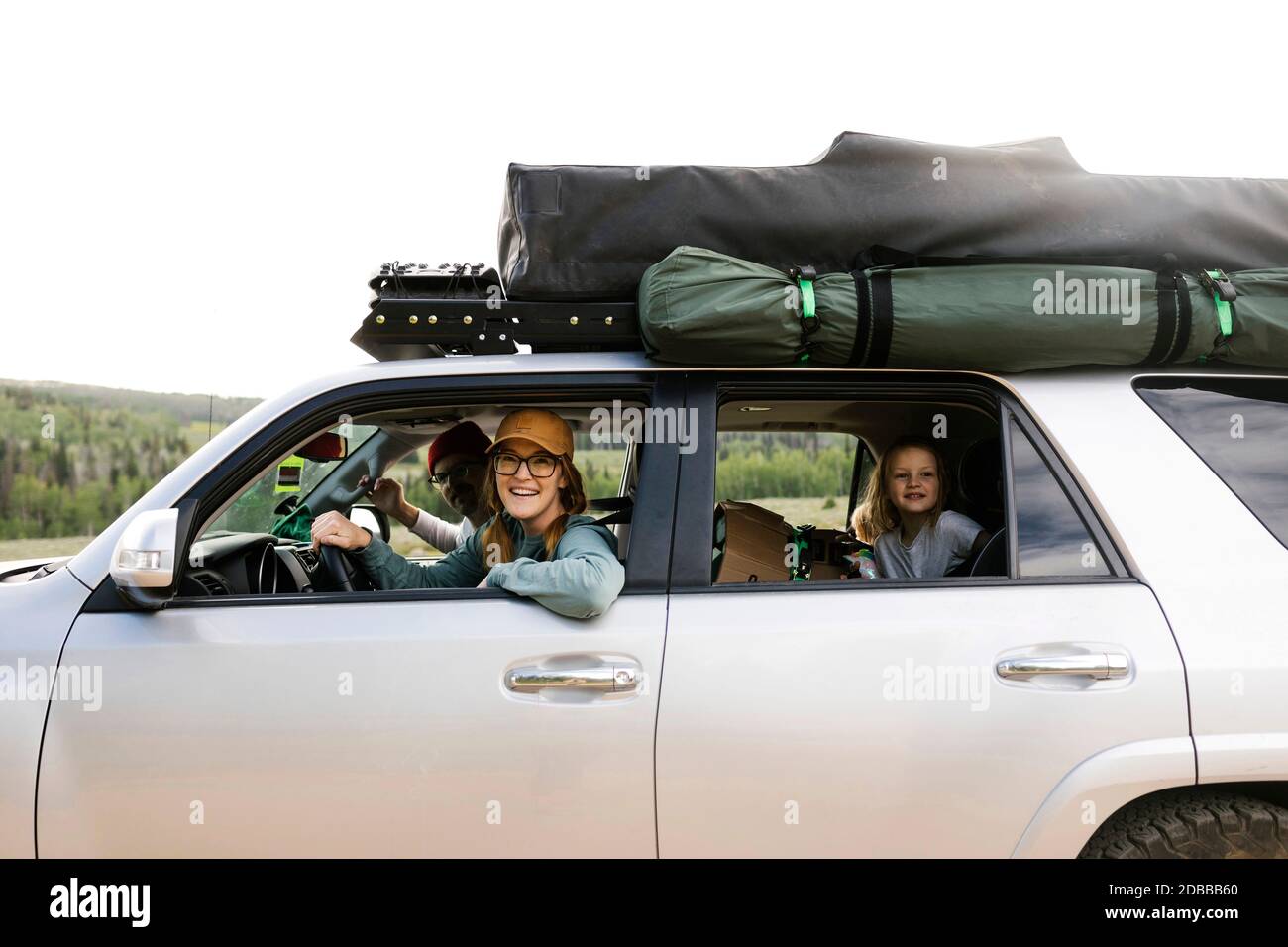 Parents with daughter (6-7) sitting in off road car with tent on roof Stock Photo