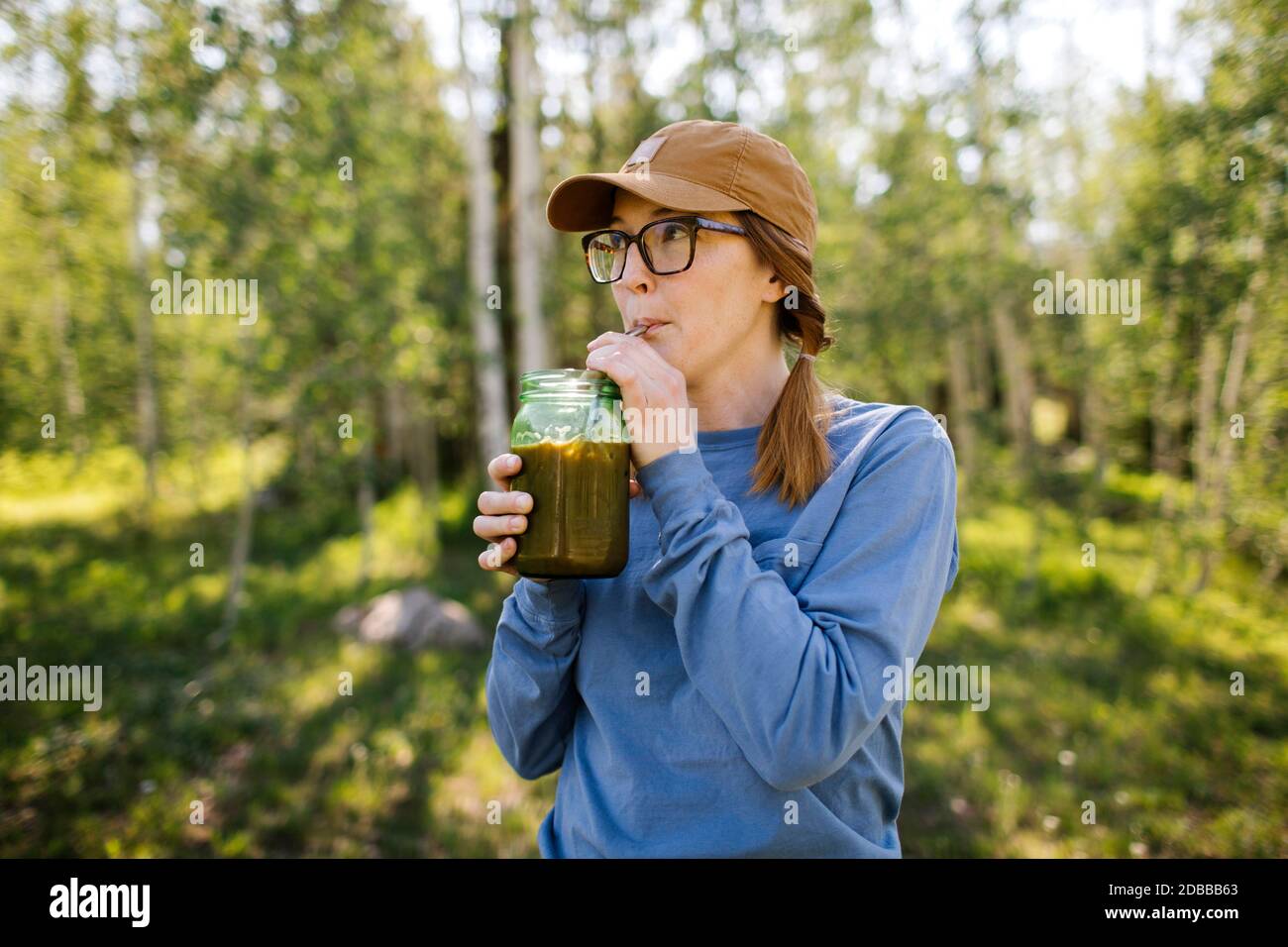 USA, Utah, Uinta National Park, Woman wearing eyeglasses and baseball cap drinking coffee from jar in forest Stock Photo