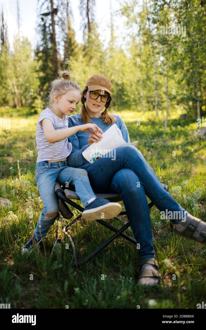 USA, Utah, Uinta National Park, Mother and daughter (6-7) doing crossword in meadow in forest Stock Photo