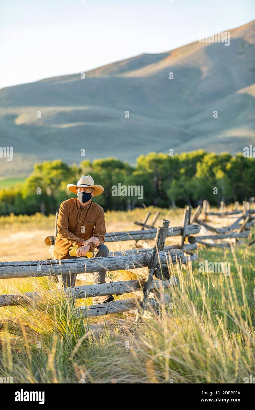 USA, Idaho, Bellevue, Rancher in face mask leaning against fence on field Stock Photo