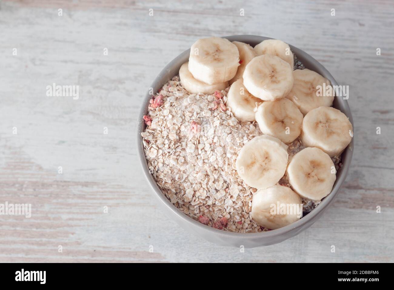 Bowl of dry oat flakes oatmeal with dry berries and sliced fresh banana on wooden table. Top view with copy space. Simple healthy breakfast. Stock Photo