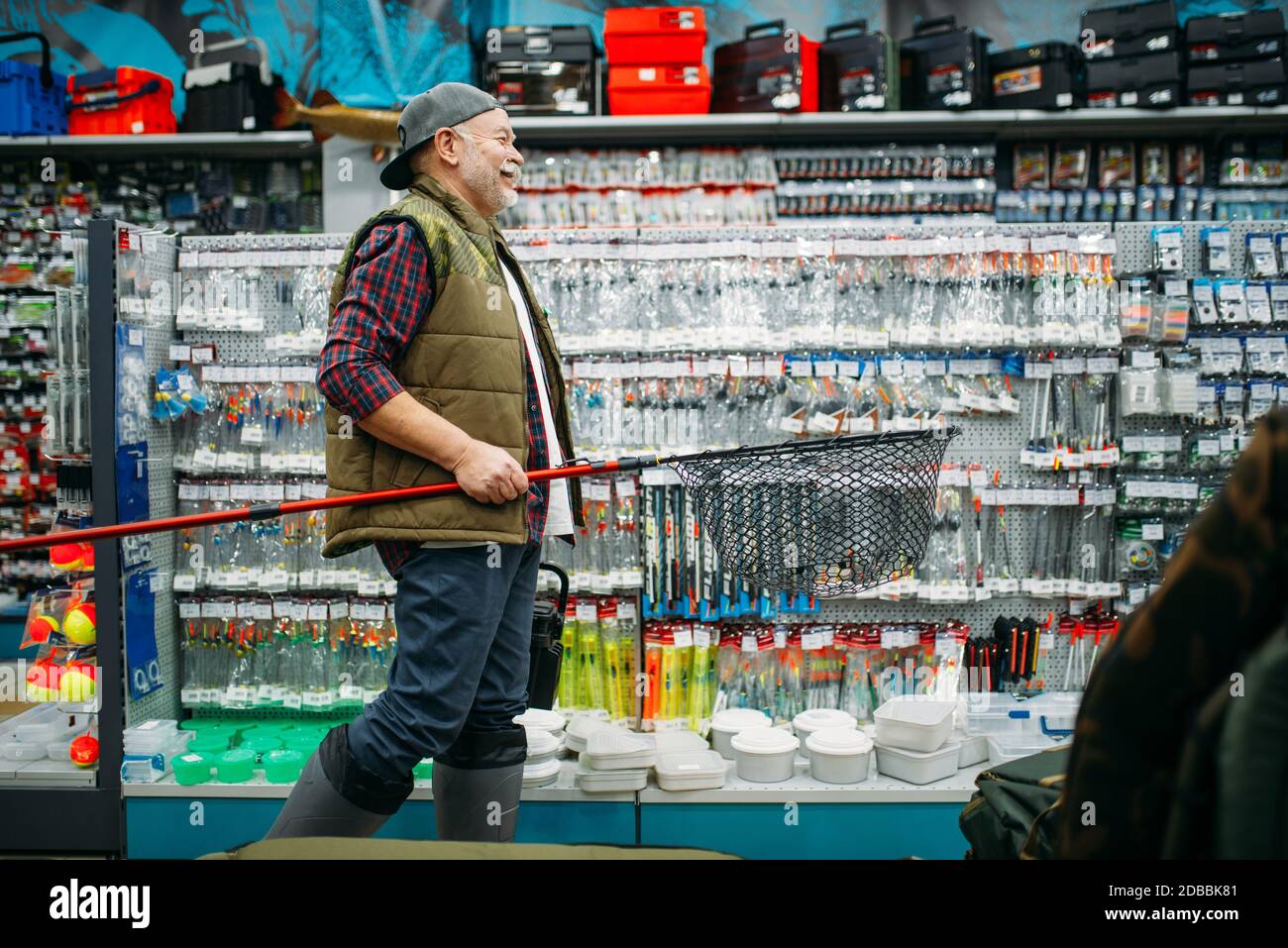 Fisherman with net and toolbox in fishing shop, hooks and baubles