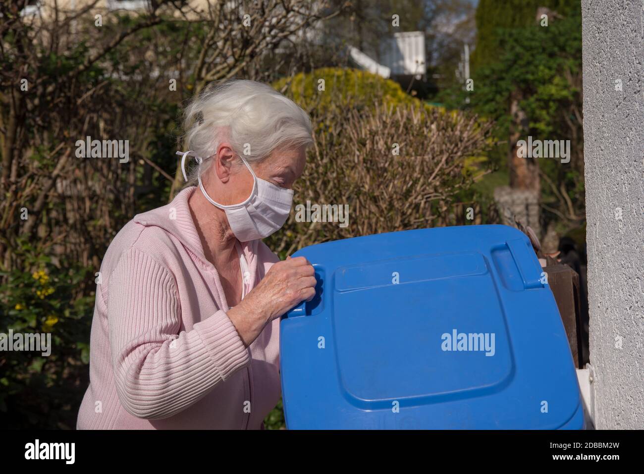 Senior woman with face mask opening garbage can Stock Photo