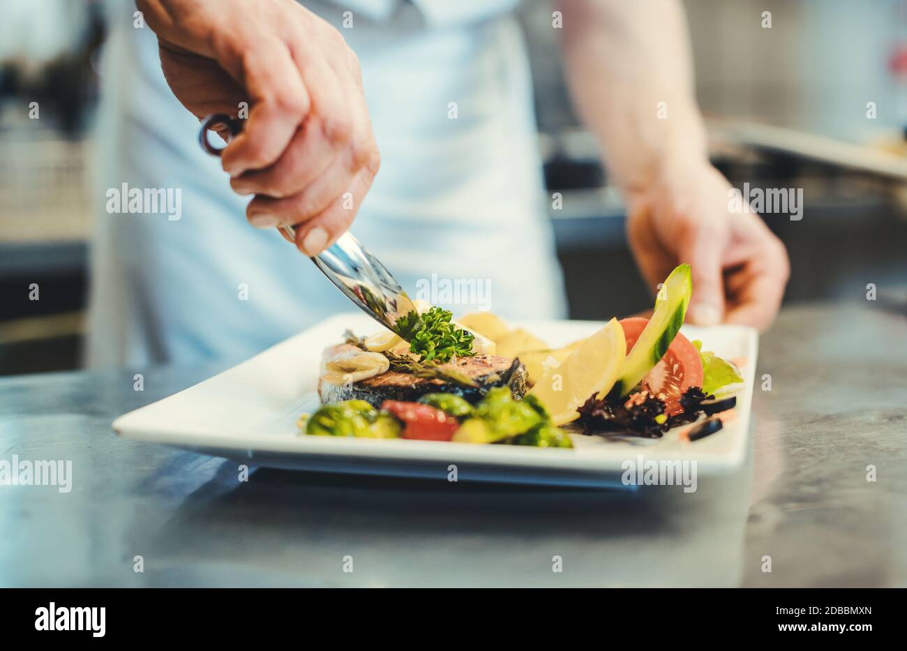 Proud chef garnishing an almost finished dish in the restaurant with leave of herbs Stock Photo