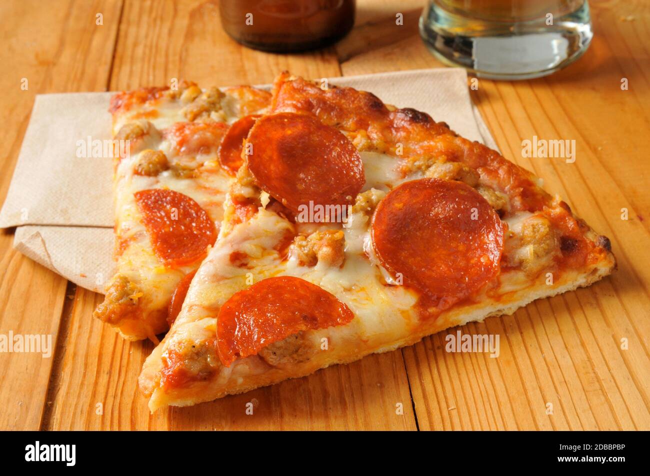 Slices of pepperoni and sausage pizza on a rustic wood table with beer