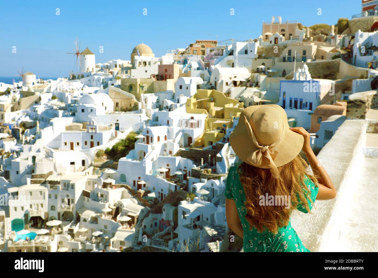 Amazing Santorini. European Holidays. Back view young woman enjoying panoramic view of the Oia village from a terrace in Santorini, Greece. Stock Photo