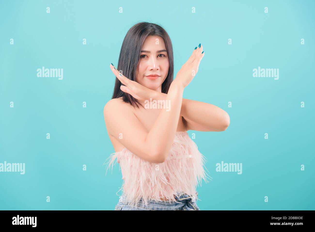 Asian happy portrait beautiful young woman standing to show say no hand sign and looking to camera isolated on blue background with copy space for tex Stock Photo