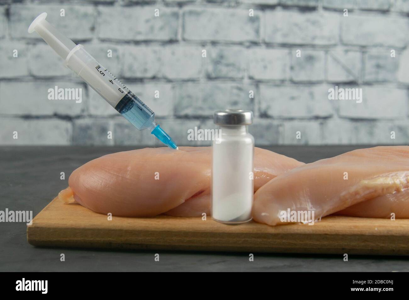 Injection syringe in raw chicken pieces, concept of injection of GMOs into the meat. Closeup