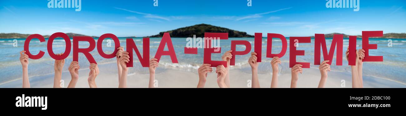 People Hands Holding Red German Word Corona Epidemie Means Corona Epidemic. Ocean And Beach As Background Stock Photo