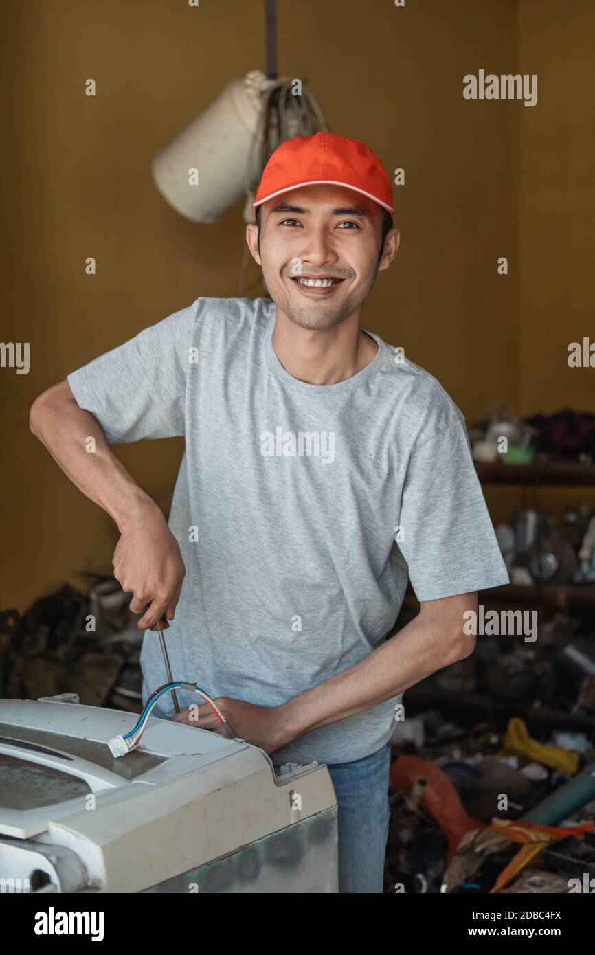 electronics workers smile at the camera using a screwdriver while repairing a washing machine at work Stock Photo