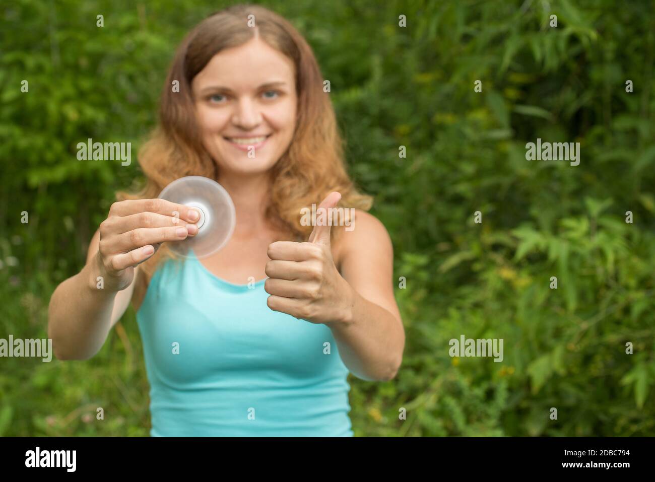 Young beautiful brunette girl smiles and fools around with moving spinners in hands in summer Stock Photo