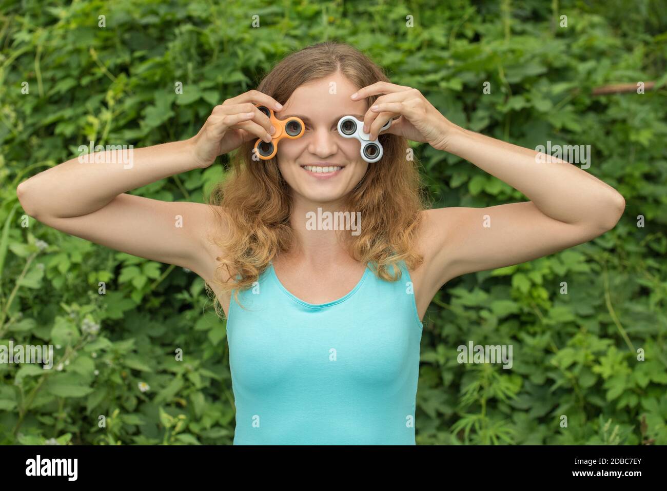 Young beautiful brunette girl smiles and fools around with moving spinners in hands in summer Stock Photo