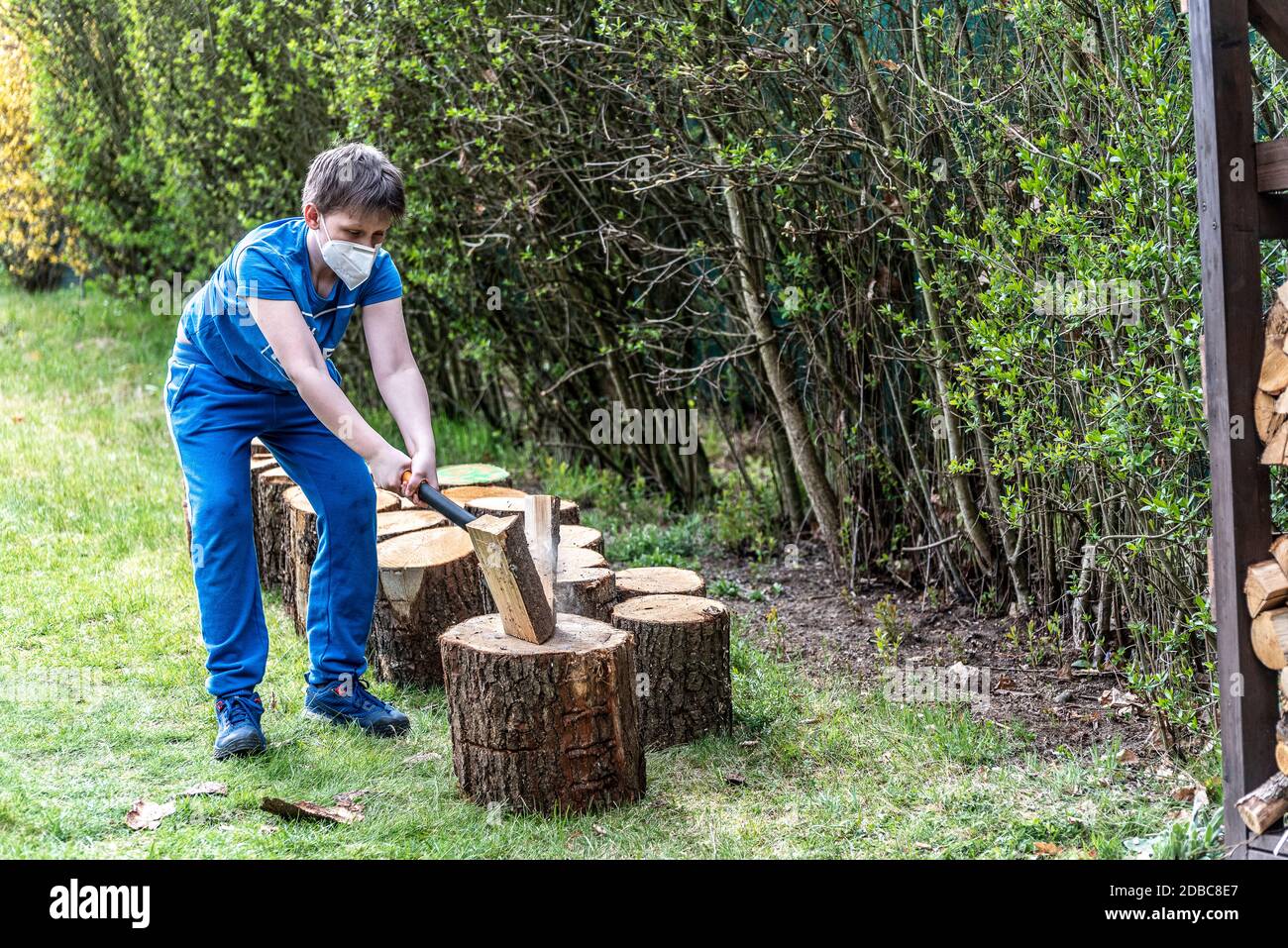 Boy chops wood wearing protective face mask Stock Photo